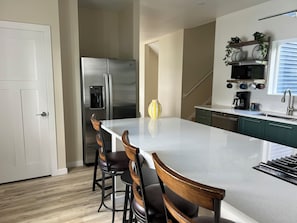 A modern kitchen with a stainless steel refrigerator, a built-in coffee maker, and a bar stool seating arrangement.