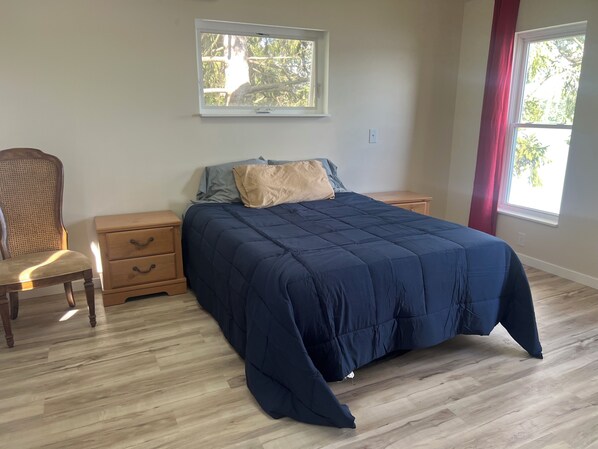 A bedroom with a bed, nightstands, a chair, and a window with curtains.