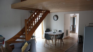 Amplia sala de estar con una escalera de madera, una mesa de comedor con sillas y un sofá.