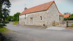 Un edificio de piedra con techo de tejas rojas, camino de entrada pavimentado y puerta de madera.