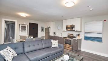 A modern living room with a grey sofa, a coffee table, and a kitchen area with a microwave and oven.