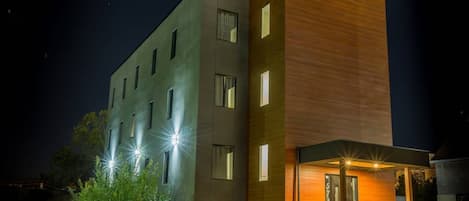 A modern multi-story building with illuminated windows and a well-lit entrance.