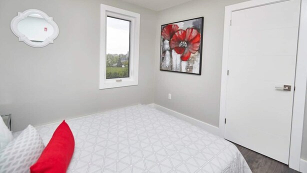 Um quarto com uma cama, janela, porta, espelho e um quadro.