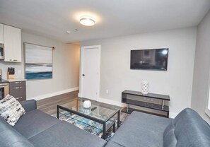 A modern living room with a glass coffee table, grey sofas, a flat-screen TV, and a painting on the wall. - This condo is perfect for families, friend groups and couples. (Niagara Falls)