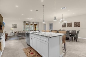 A spacious kitchen with a large island, pendant lighting, and a dining area with a table and chairs. - Promotion! 8BR Disney Villa | Pool, Spa, Game Room (Kissimmee)