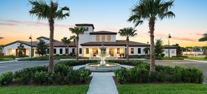 A two-story building with a central fountain, surrounded by palm trees and well-maintained landscaping. - Promotion! 8BR Disney Villa | Pool, Spa, Game Room (Kissimmee)