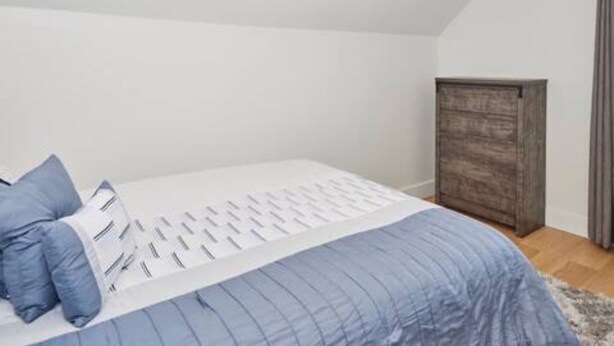 Ein Schlafzimmer mit Bett, Kissen, einem Kleiderschrank und einem Fenster mit Vorhängen.