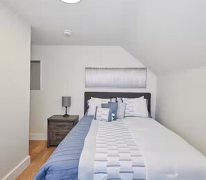 A bedroom with a bed, a nightstand, a lamp, and a window. - Fully renovated 3-bedroom home with 3 beds, 1 sofa bed, and 1 bathroom. Sleeps families and groups comfortably. Just a short walk to Clifton Hill, Niagara Falls, restaurants, attractions, and entertainment. (NIAGARA FALLS)
