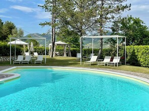 Ein Schwimmbad mit Liegestühlen und Sonnenschirmen, umgeben von viel Grün und Hügeln.