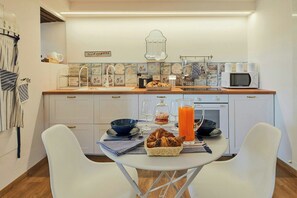 Eine moderne Küche mit weißen Schränken, einer Holz Arbeitsplatte, einer Mikrowelle und einem Esstisch, gedeckt mit einem Brotkorb, einem Glas Orangensaft und Weingläsern.