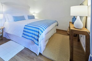 Ein ordentlich gemachtes Bett mit einer gestreiften Tagesdecke, einer Nachttischlampe und einem kleinen Tisch mit einer Vase.