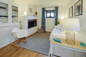 Ein Wohnzimmer mit Kamin, weißen Möbeln, einem gemusterten Teppich und einem Fenster mit Vorhängen.