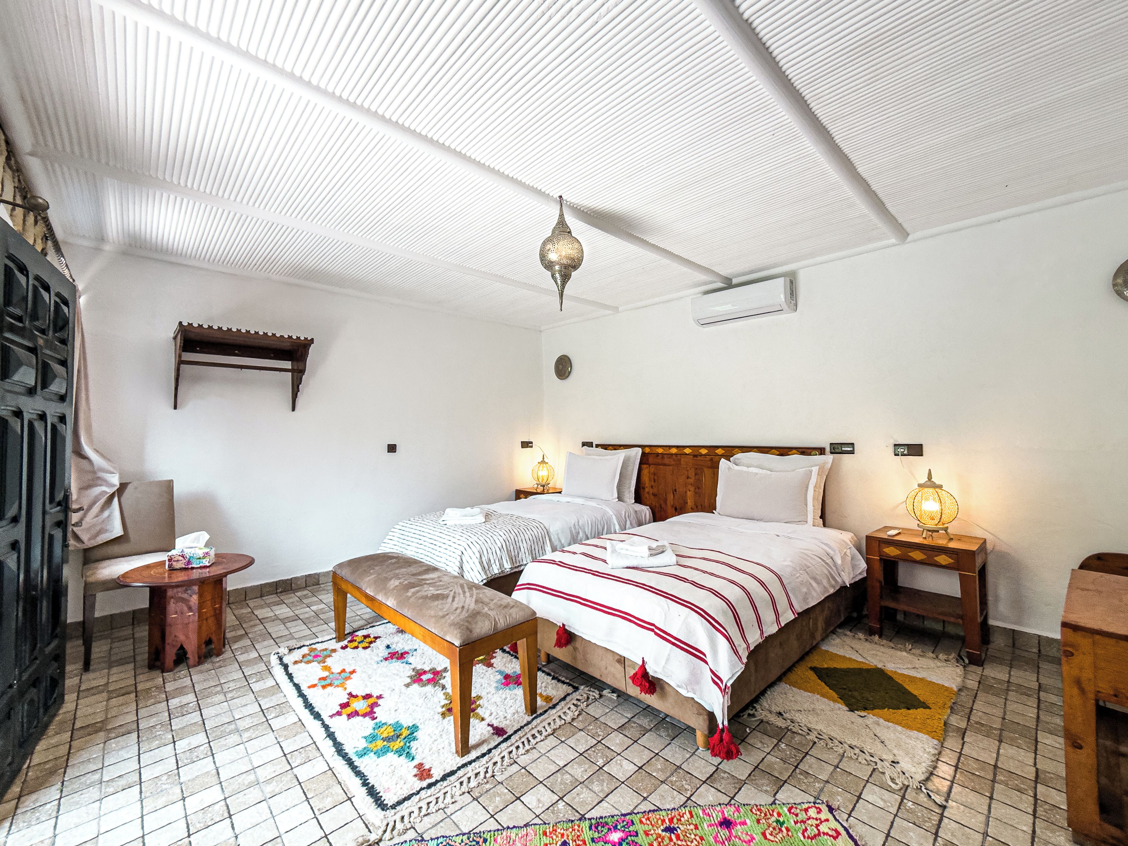 Une chambre à coucher avec un lit, des tables de chevet, un banc, un tapis et un ventilateur de plafond.