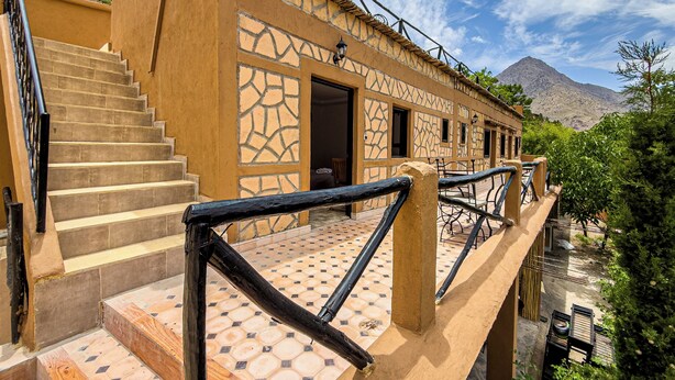 A building with a staircase leading to a balcony, surrounded by greenery and a mountain in the background. - Tonaroz House (Tamatert)