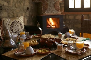 A traditional meal setup with a firewood stove in the background, a woven mat table, and various dishes and utensils.