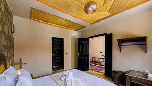 A hotel room with a bed, a small table, a bench, and a door leading to a balcony. - Tonaroz House (Tamatert)