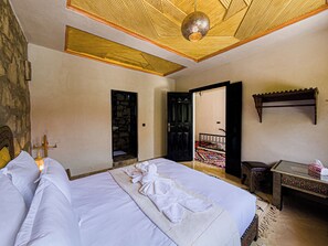 Habitación de hotel con cama, una mesita, un banco y una puerta que da a un balcón.