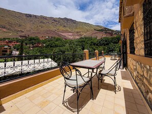 A balcony with a table and chairs, overlooking a mountainous landscape with buildings in the distance. - Tonaroz House (Tamatert)