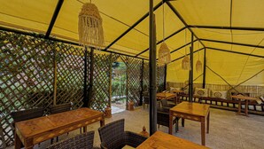 A tented dining area with tables and chairs, a lattice wall, and hanging light fixtures. - Tonaroz House (Tamatert)