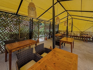 Un área de comedor cubierta con mesas y sillas, una pared con celosía y lámparas colgantes.