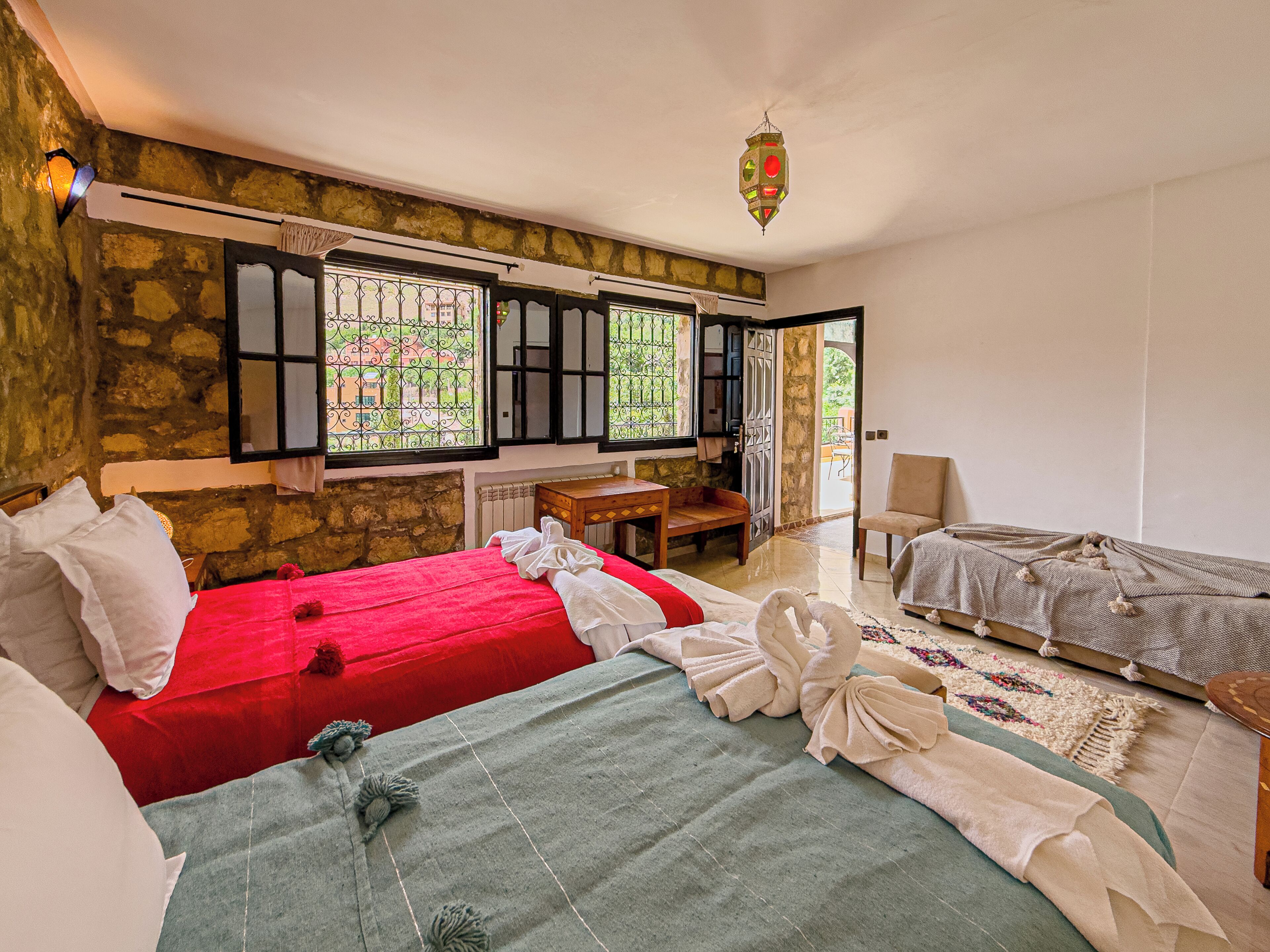 Una habitación con dos camas, un escritorio de madera, una silla y vista a través de una ventana con rejas.