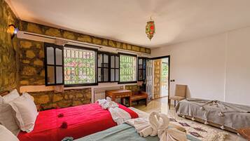 Una habitación con dos camas, un escritorio de madera, una silla y vista a través de una ventana con rejas.