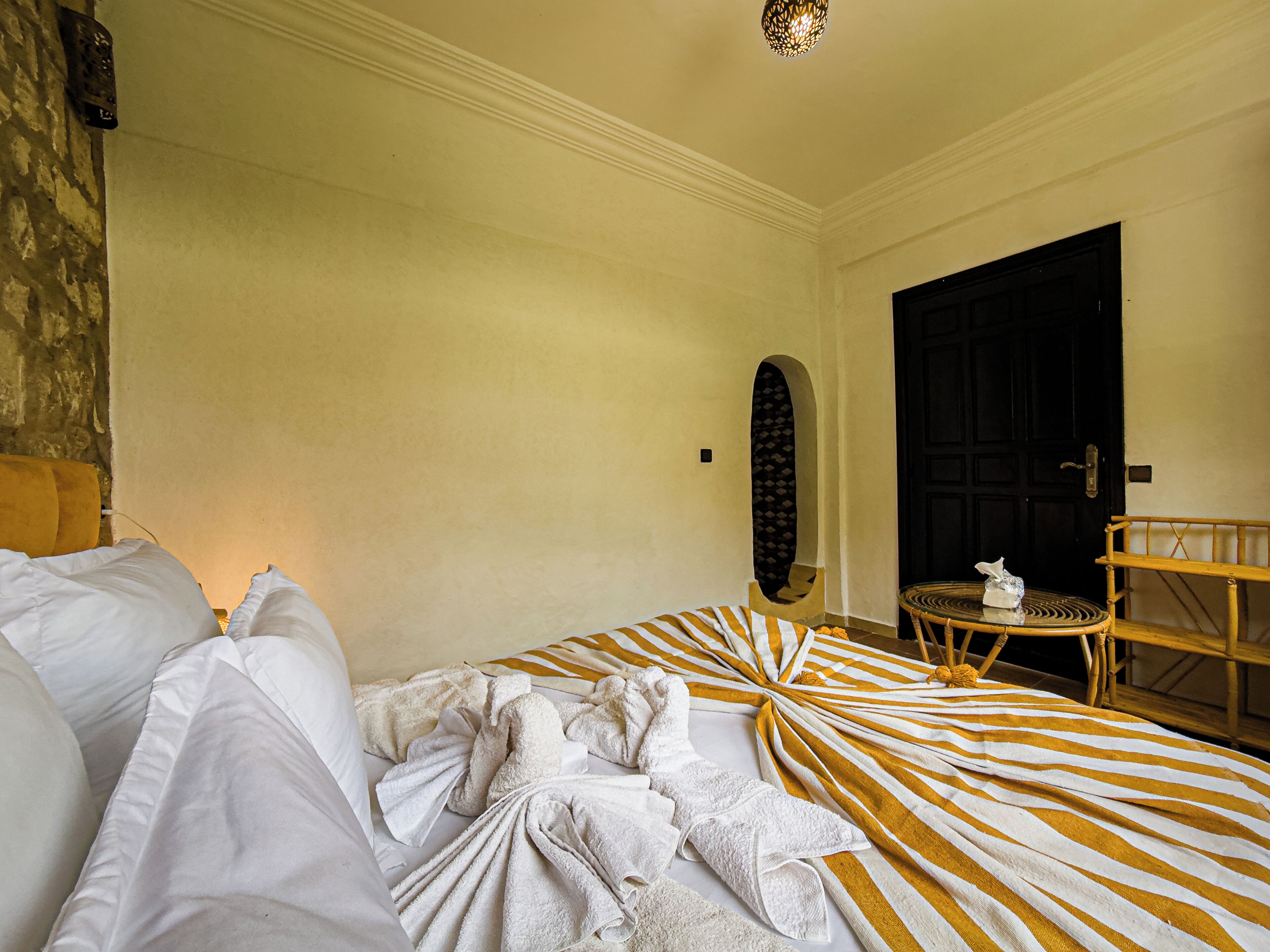 Une chambre d’hôtel avec un lit, une table ronde, une chaise, une porte et un mur orné d’un motif texturé.