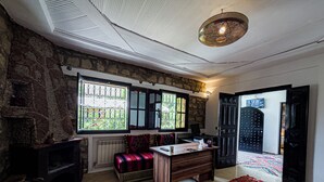 A room with a stone wall, a wooden bench, a desk, and a patterned rug. - Tonaroz House (Tamatert)