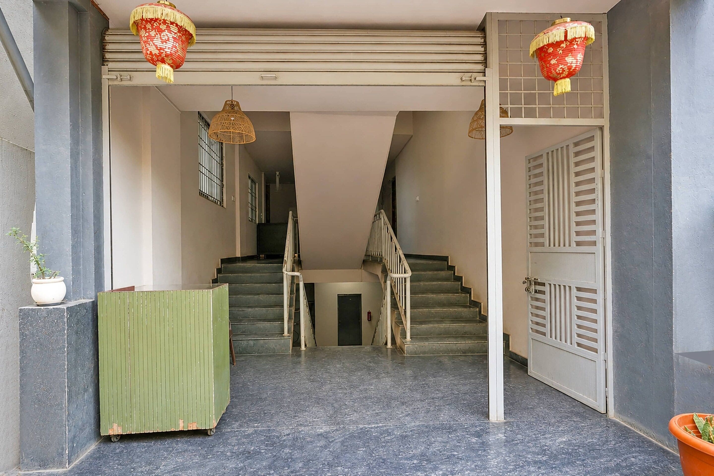 Un escalier menant à un palier où se trouvent un banc vert et un pot de fleurs sur la gauche.