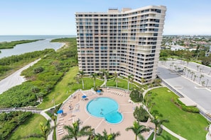 Ein Hochhotel mit Swimmingpool, umgeben von viel Grün und Blick aufs Meer.