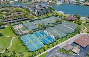 Eine Vogelperspektive eines Hotelkomplexes mit mehreren Tennisplätzen, einem Yachthafen und umgebender Grünfläche.