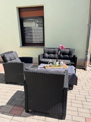 Un espace extérieur aménagé avec des meubles en osier et une table décorée d’un arrangement floral.