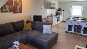 Una sala de estar moderna con un sofá seccional, una mesa de centro y un comedor, con una cocina al fondo.