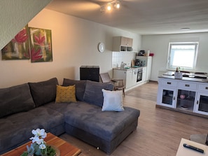 A modern living room with a sectional sofa, a coffee table, and a dining area with a kitchen in the background. - Westerhäuser Vacation Rentals - Bergzauber Apartment - Hiking in the Harz Mountains (Thale)