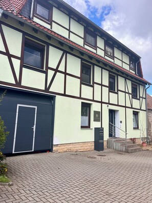 A traditional half-timbered building with a garage, a staircase, and a paved courtyard. - Westerhäuser Vacation Rentals - Bergzauber Apartment - Hiking in the Harz Mountains (Thale)