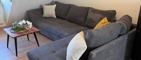 A modern living room with a grey sectional sofa, a small wooden coffee table, and a painting of flowers on the wall.