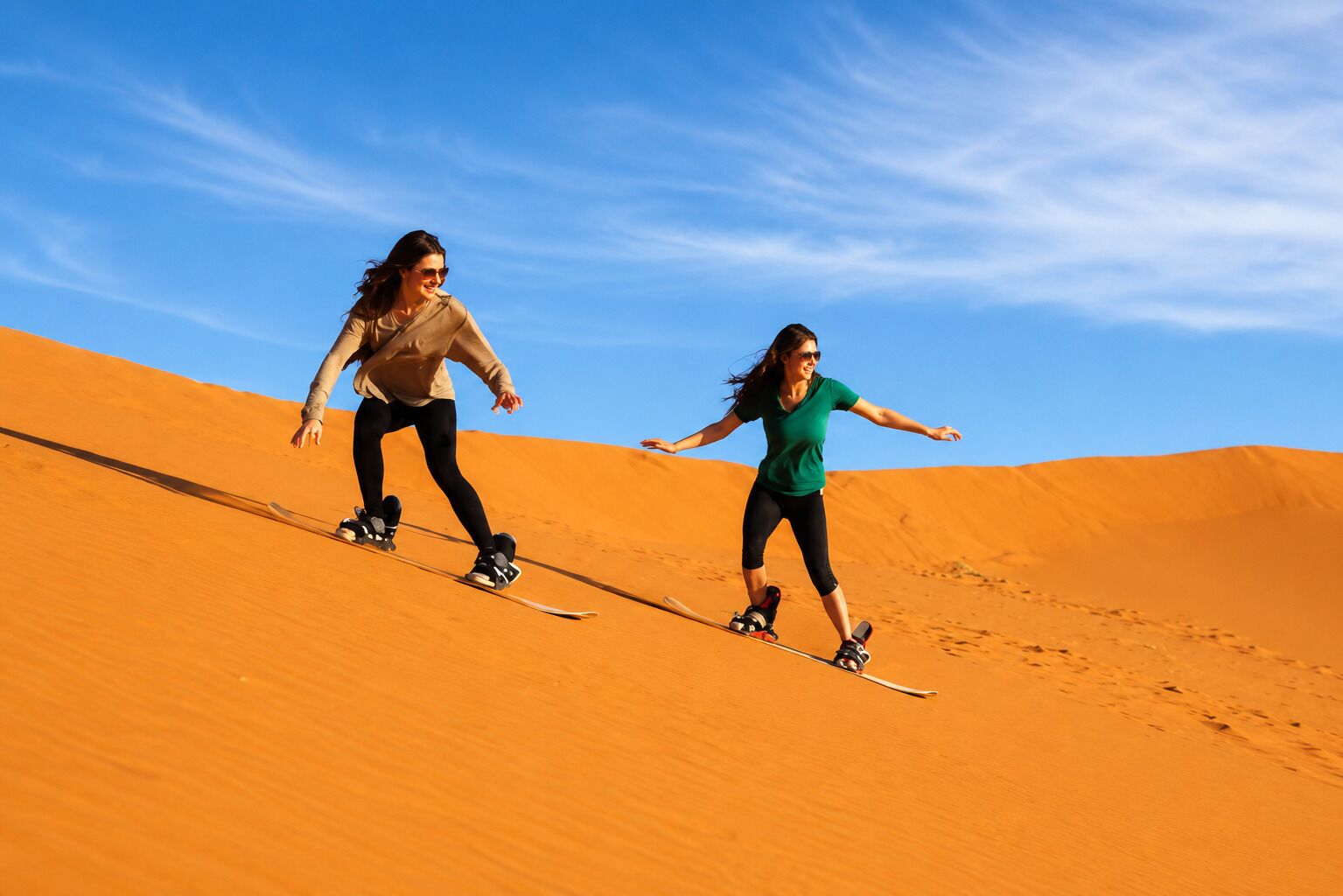 Two people skiing on sand dunes under a clear sky.