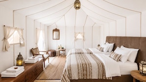 Un dormitorio tipo tienda de campaña con una cama grande, dos mesitas de noche, un aparador de madera, una silla y una pequeña mesa con objetos decorativos.