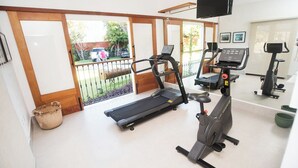 Un gimnasio en casa con cinta de correr, elíptica y bicicleta estática, un televisor montado en la pared y un gran ventanal corredizo que da a un jardín trasero.