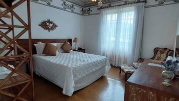 A bedroom with a large bed, a wooden chair, a desk, and a chandelier.