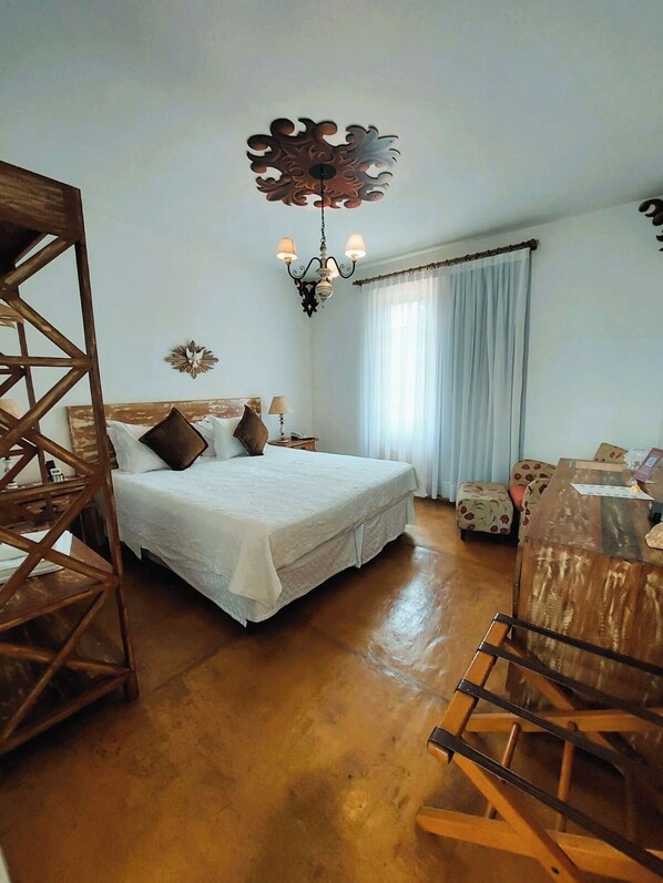 A bedroom with a bed, a wooden chair, a desk, and a chandelier.