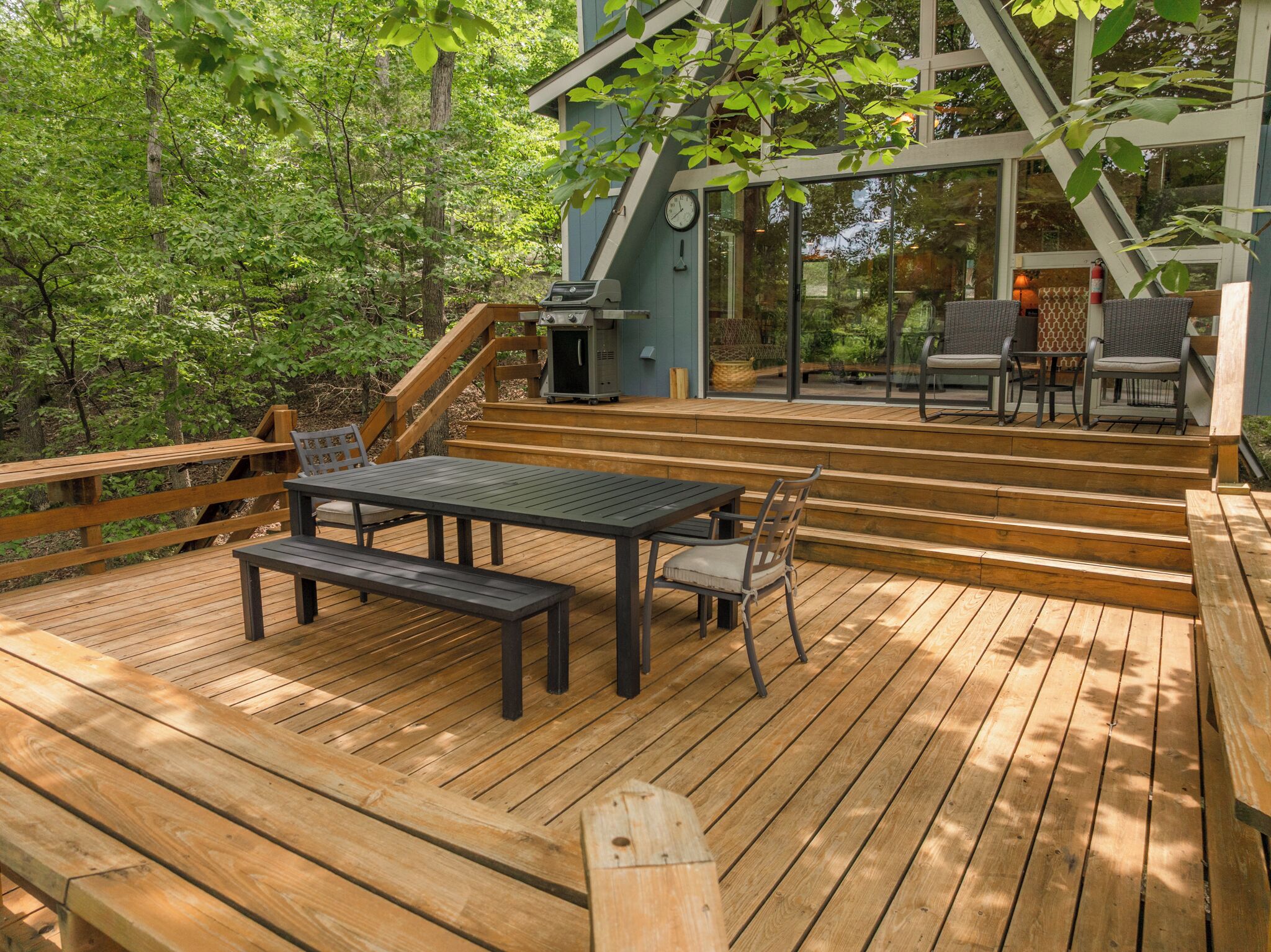 Terraza al aire libre con una mesa y sillas, rodeada por barandas de madera y árboles.