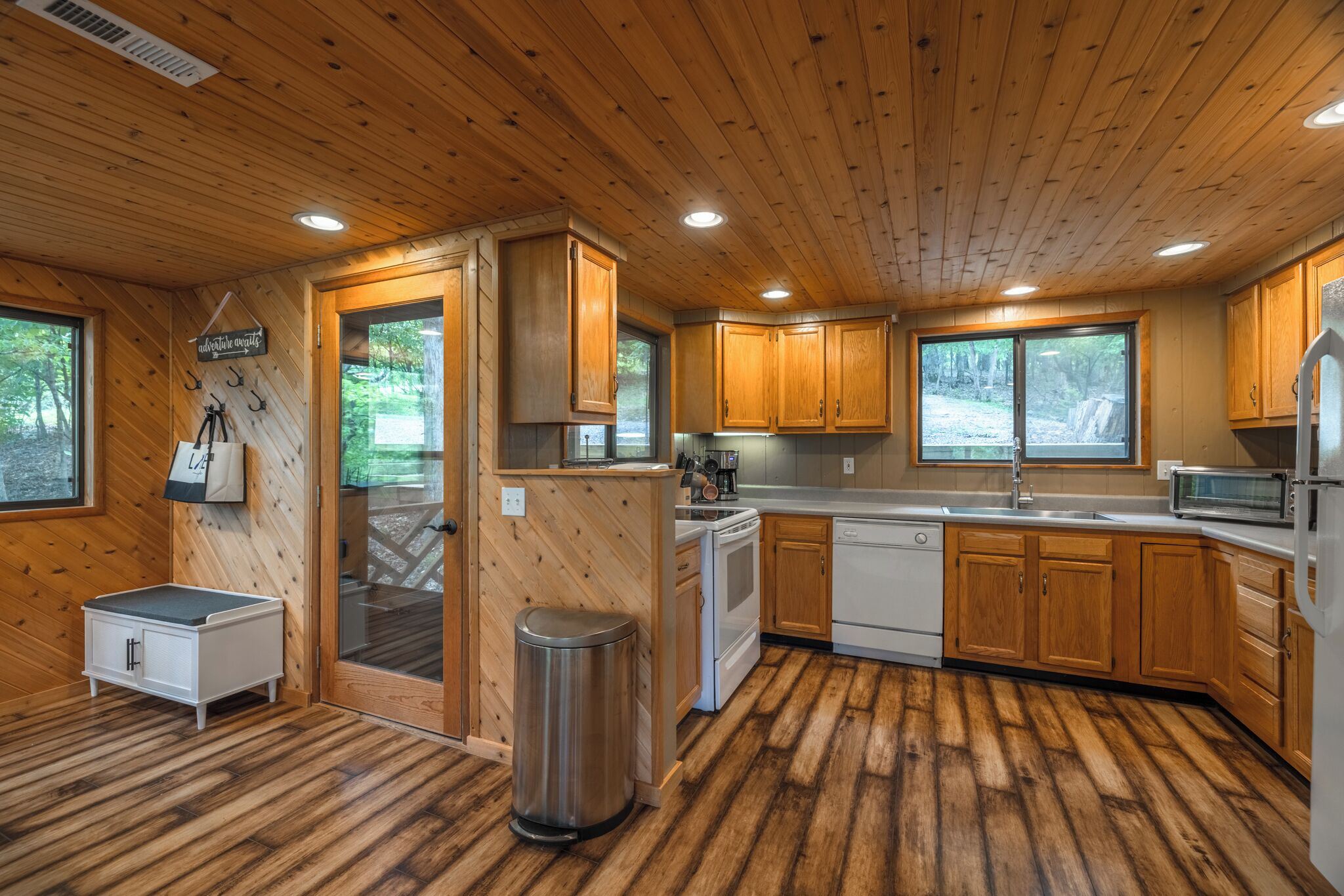 Een houten cabin met een keuken, een klein eethoekje en een vuilnisbak.