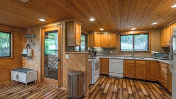 Een houten cabin met een keuken, een klein eethoekje en een vuilnisbak.