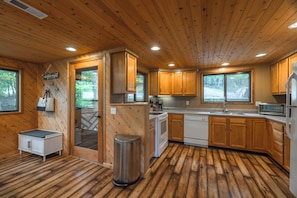 A wooden cabin interior with a kitchen, a small dining area, and a trash bin. - Lakefront Retreat by Innsbrook Vacations! (Innsbrook)