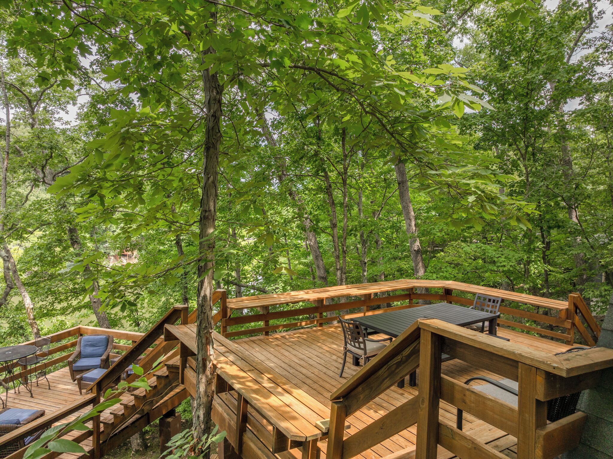 Une terrasse en bois, aménagée avec du mobilier d’extérieur, et entourée d’arbres.