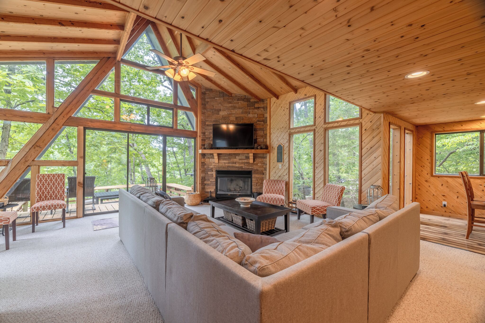A spacious living room with a large sectional sofa, a fireplace, and a television mounted on a stone wall.