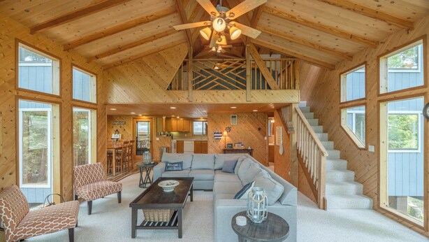 A spacious living area with a high ceiling, a staircase, and large windows.