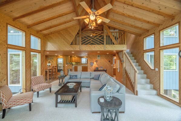 A spacious living area with a high ceiling, a staircase, and large windows.
