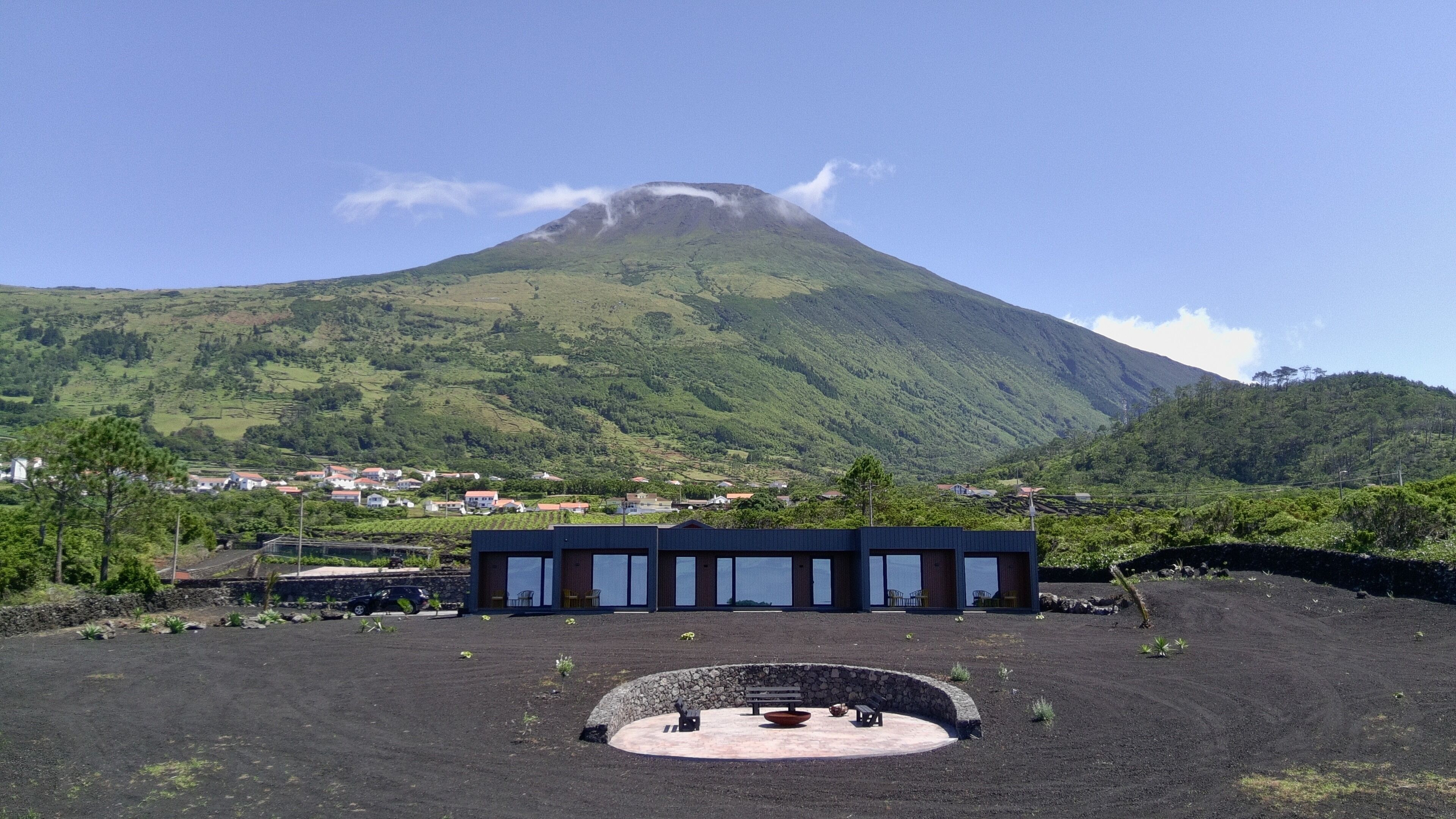 A modern building with a circular outdoor seating area, surrounded by a landscaped garden, with a mountain in the background.